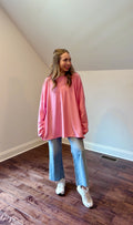 Person wearing a pink oversized sweatshirt and blue jeans standing in a room with wooden flooring.