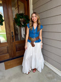 Woman in a blue top and white skirt standing outside a house.