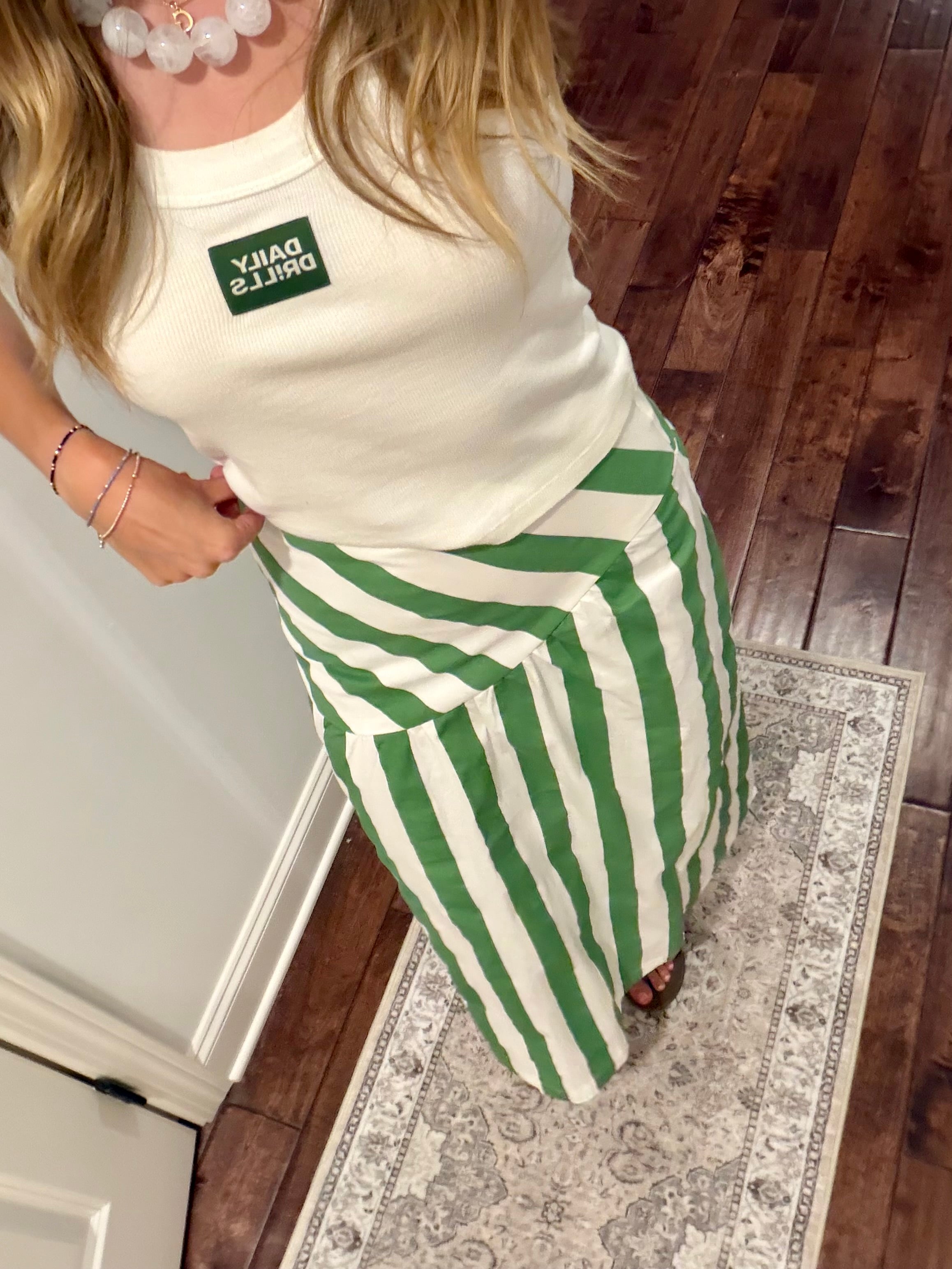 Person wearing a white top with a green logo and green and white striped pants on a wooden floor.