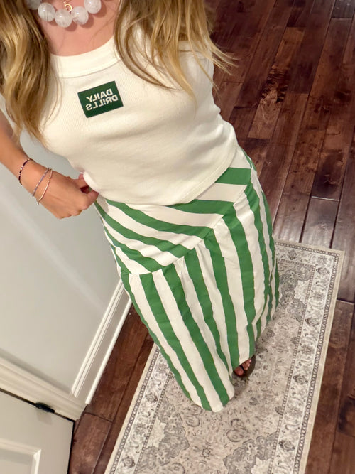 Person wearing a white top with a green logo and green and white striped pants on a wooden floor.