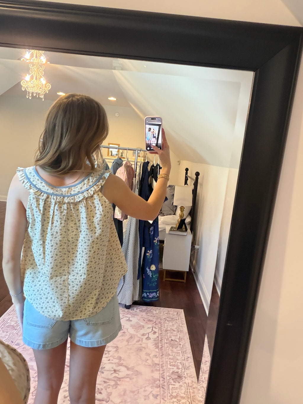 Person taking a mirror selfie wearing a patterned top and shorts in a store.