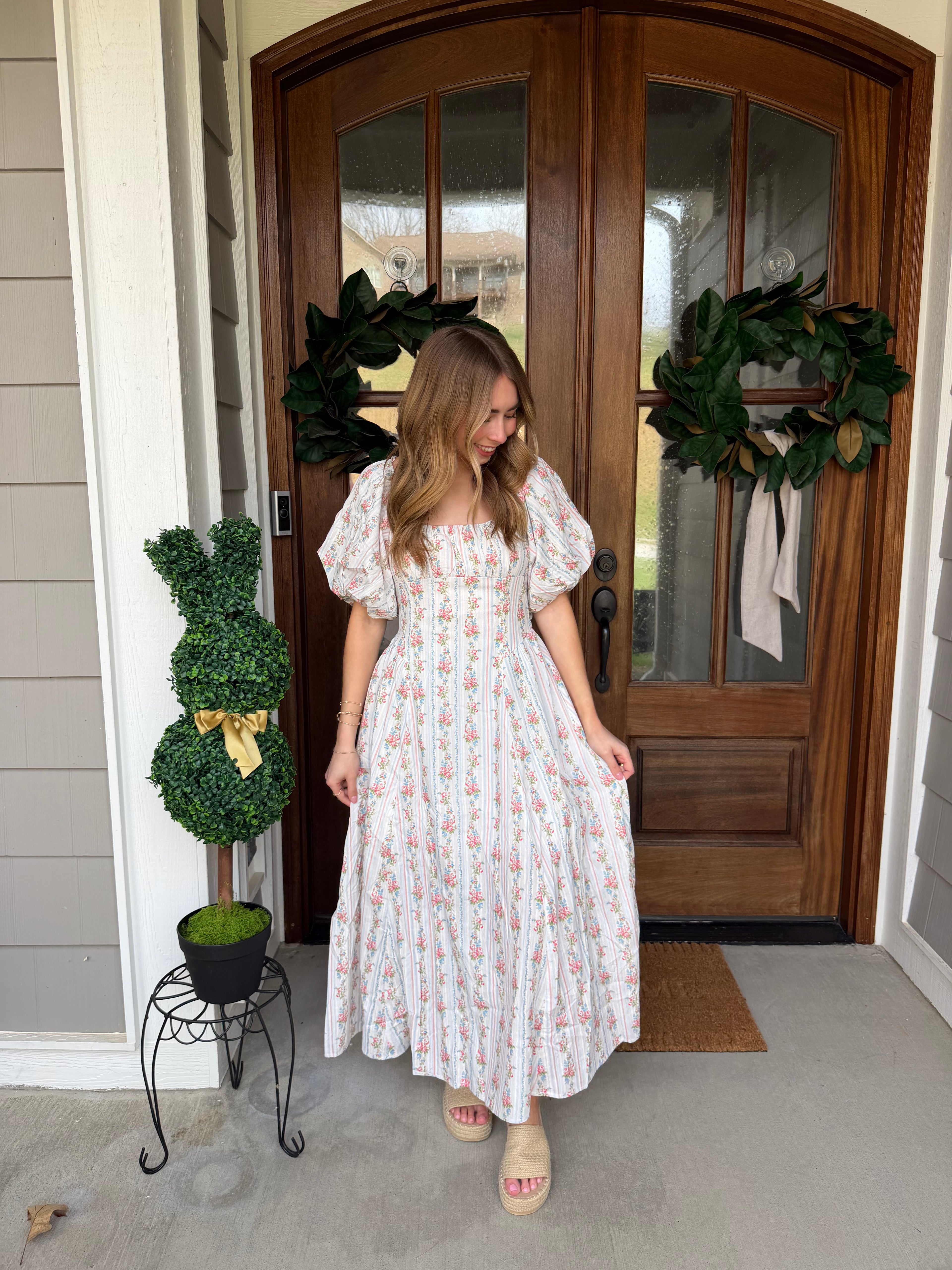Woman in a white dress standing in front of a wooden door with wreaths.