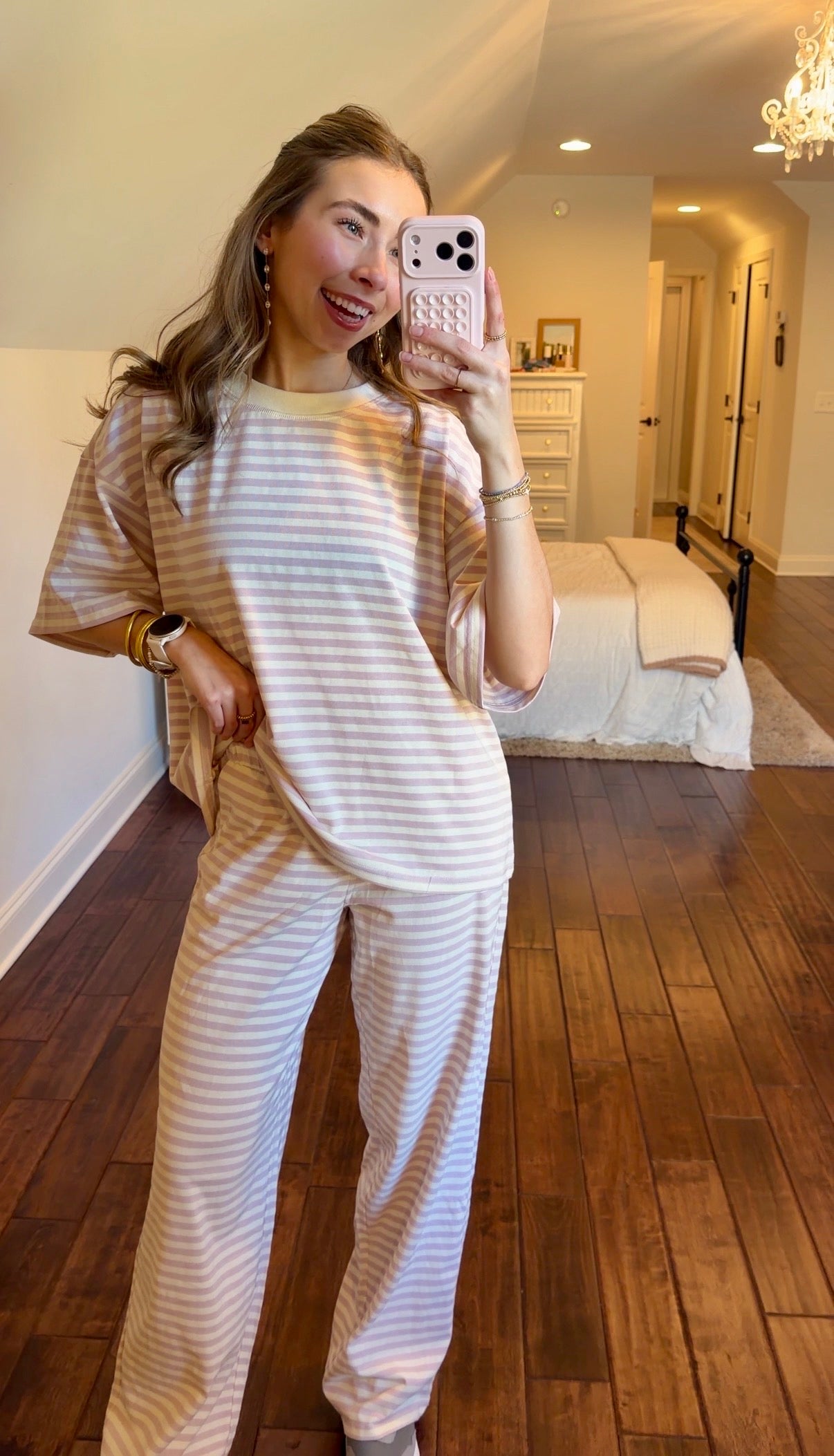 Woman taking a mirror selfie wearing a striped pink set in a bedroom.