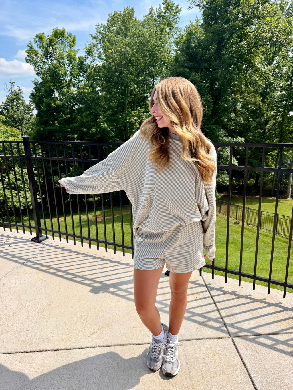 Woman in a light gray outfit standing outdoors with trees in the background