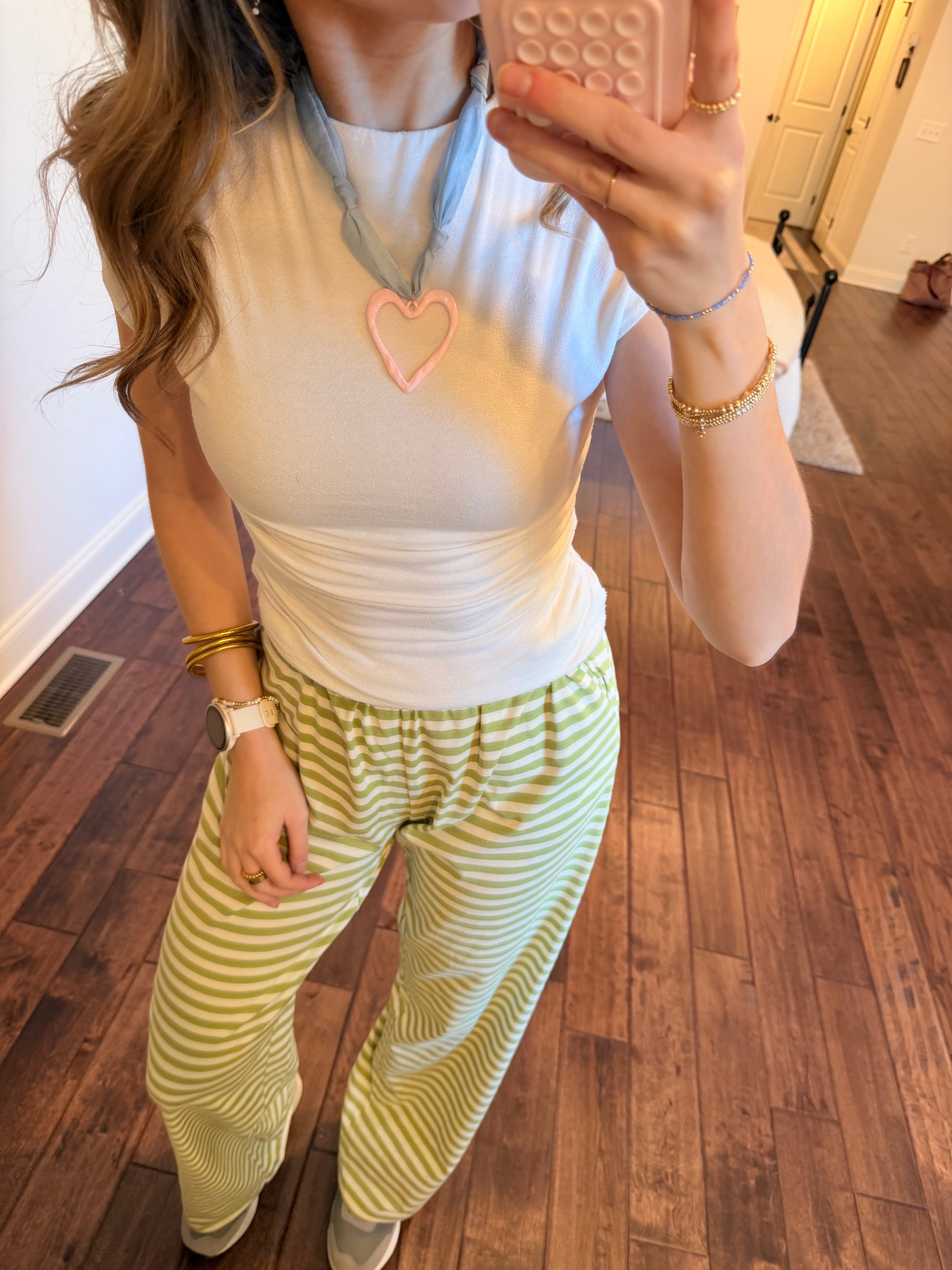Person wearing a white top and green striped pants on a wooden floor.