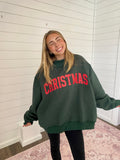 Person wearing a green sweatshirt with 'Christmas' in red text, standing in a room with white walls and a rug.
