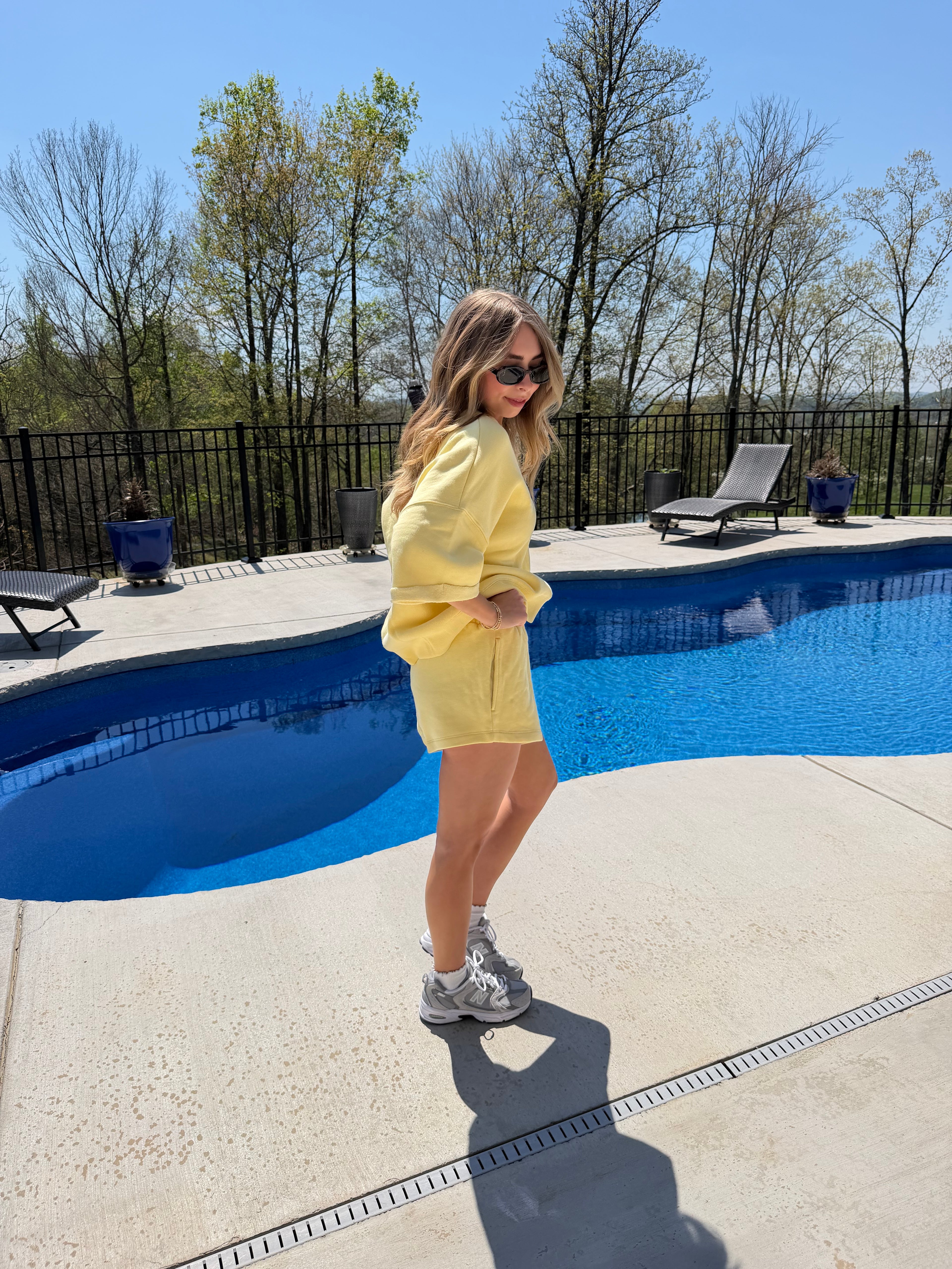 Person in a yellow outfit standing by a pool with trees and a clear sky in the background