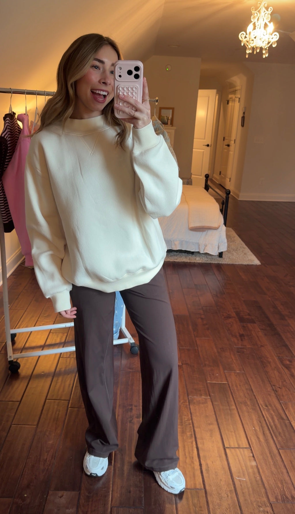 Person wearing a cream sweatshirt and brown pants in a room with wooden flooring.