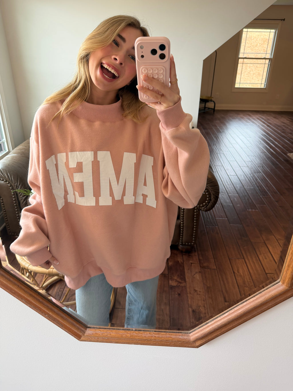 Person wearing a pink sweatshirt with white text, taking a mirror selfie.