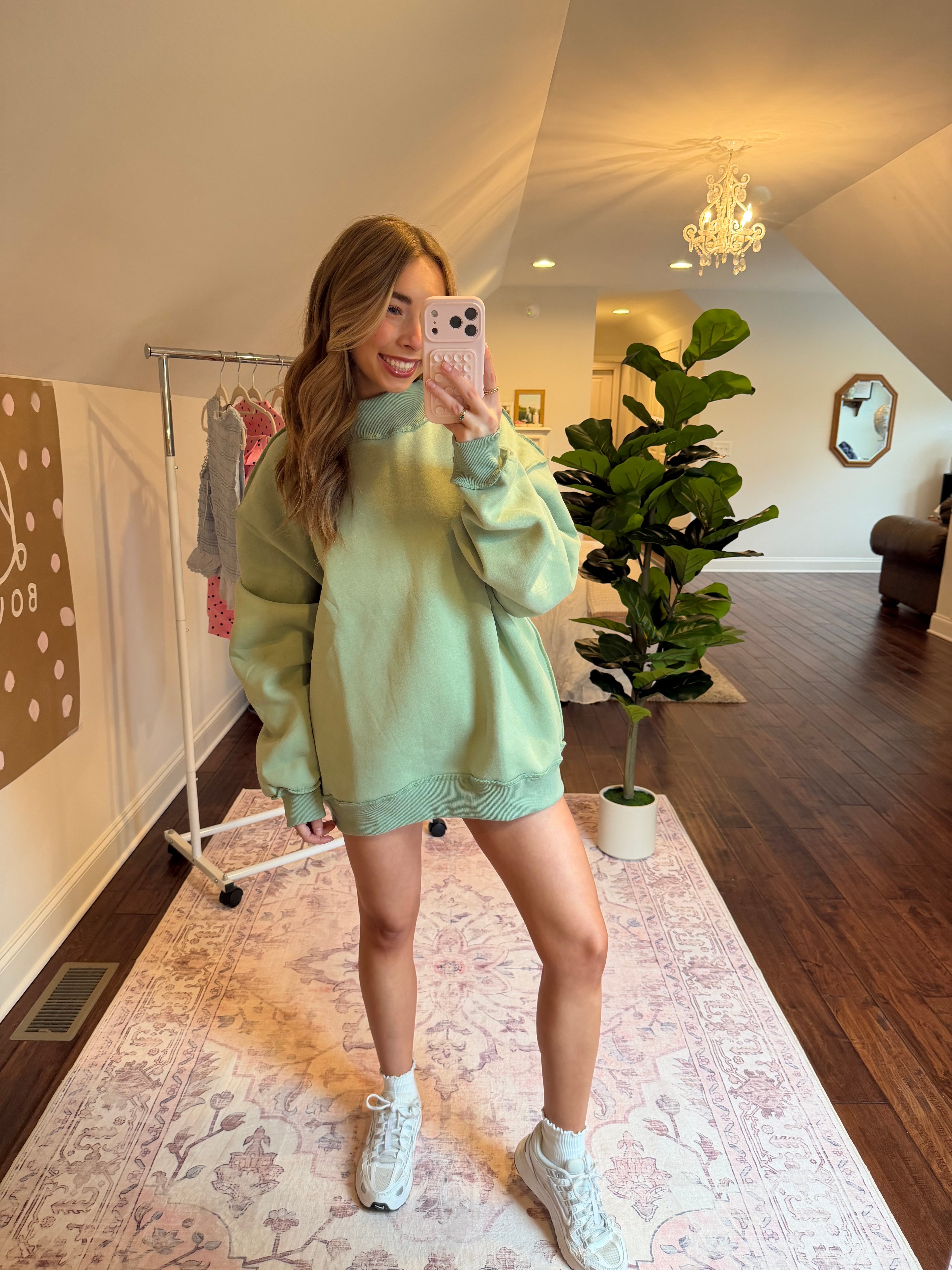 Person wearing a light green sweater and white sneakers in a room with a plant and mirror.