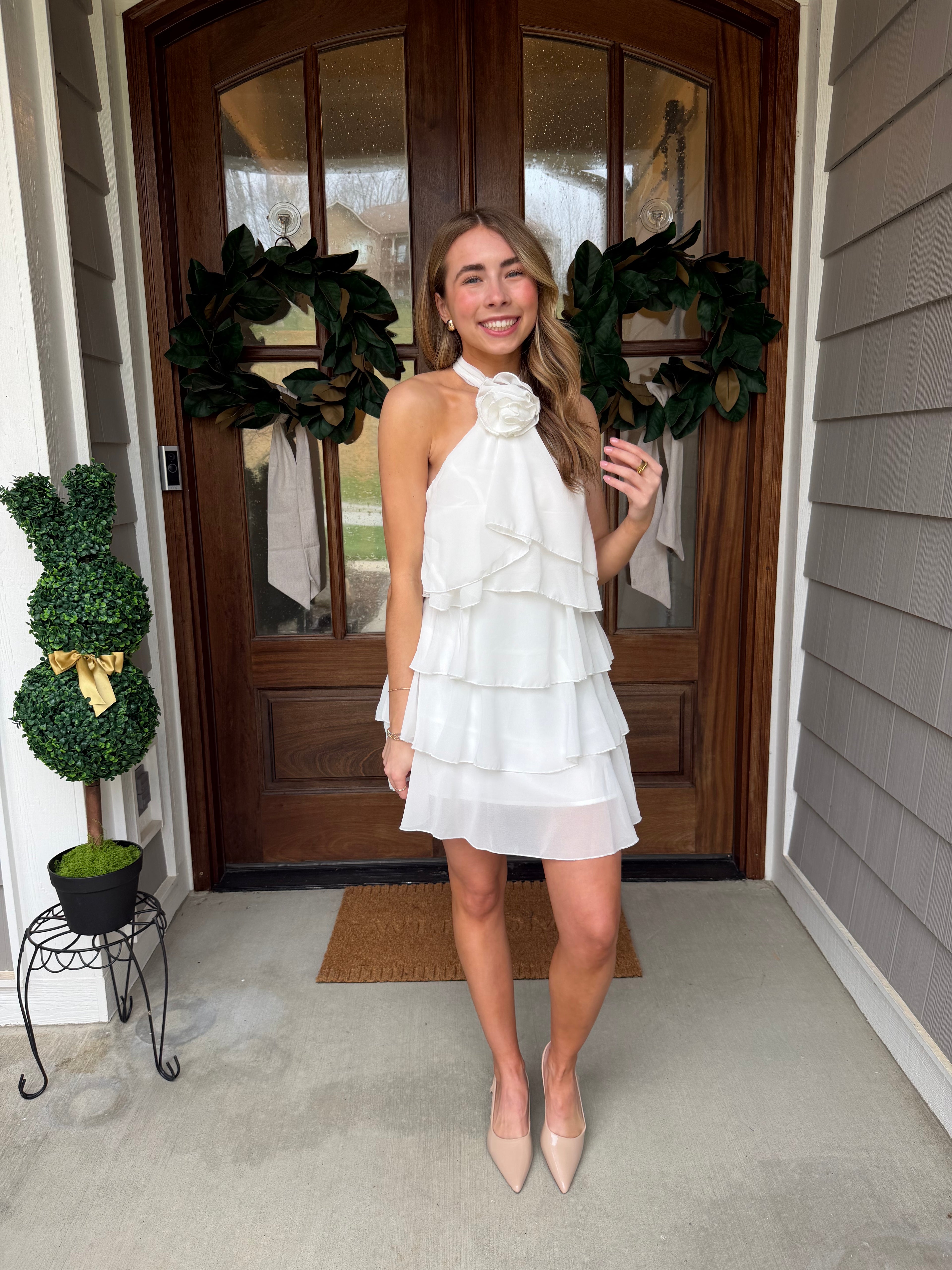 Woman in a white dress standing in front of a wooden door with wreaths.