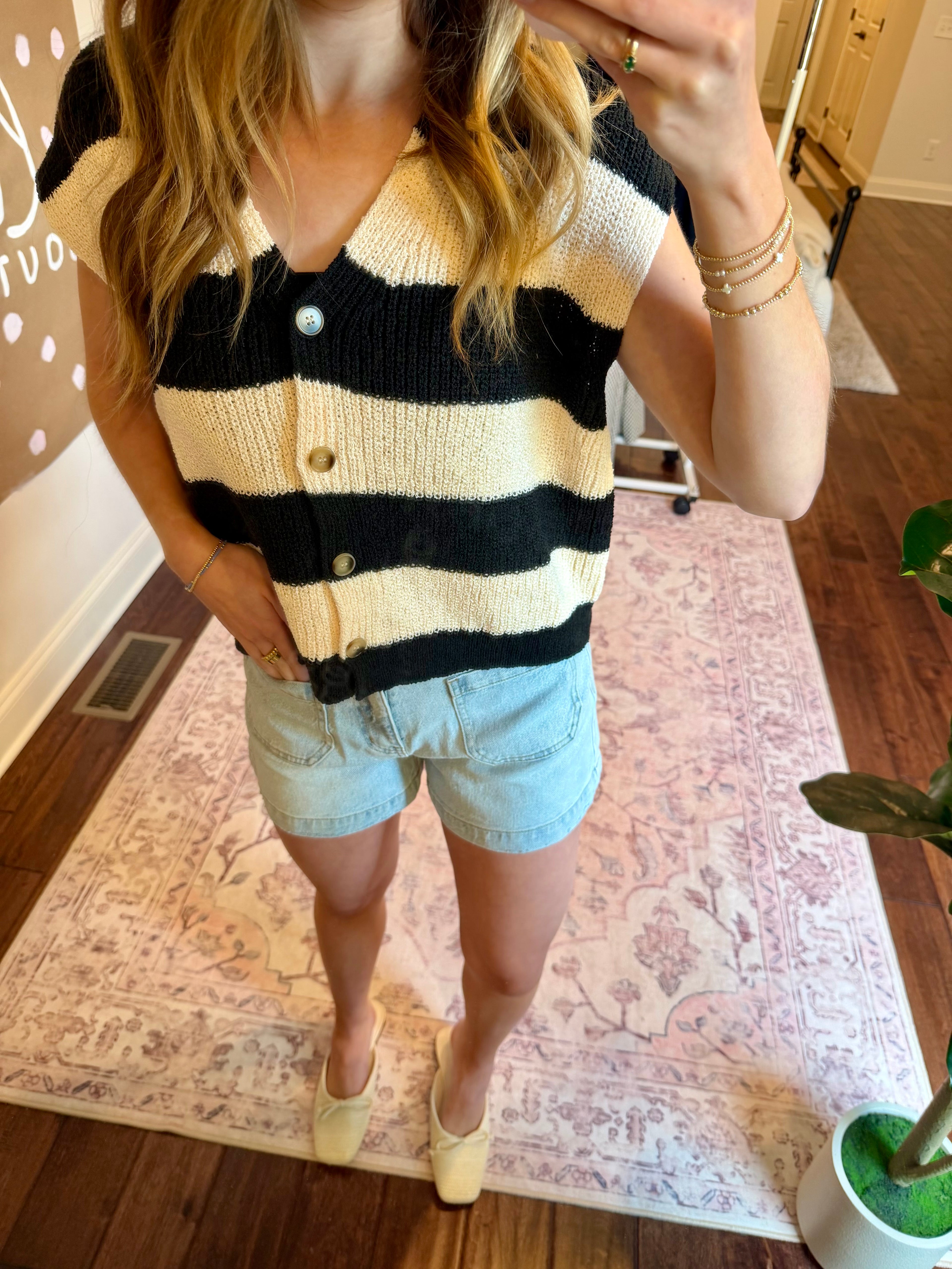 Woman taking a mirror selfie wearing a striped sweater and denim shorts in a home setting.