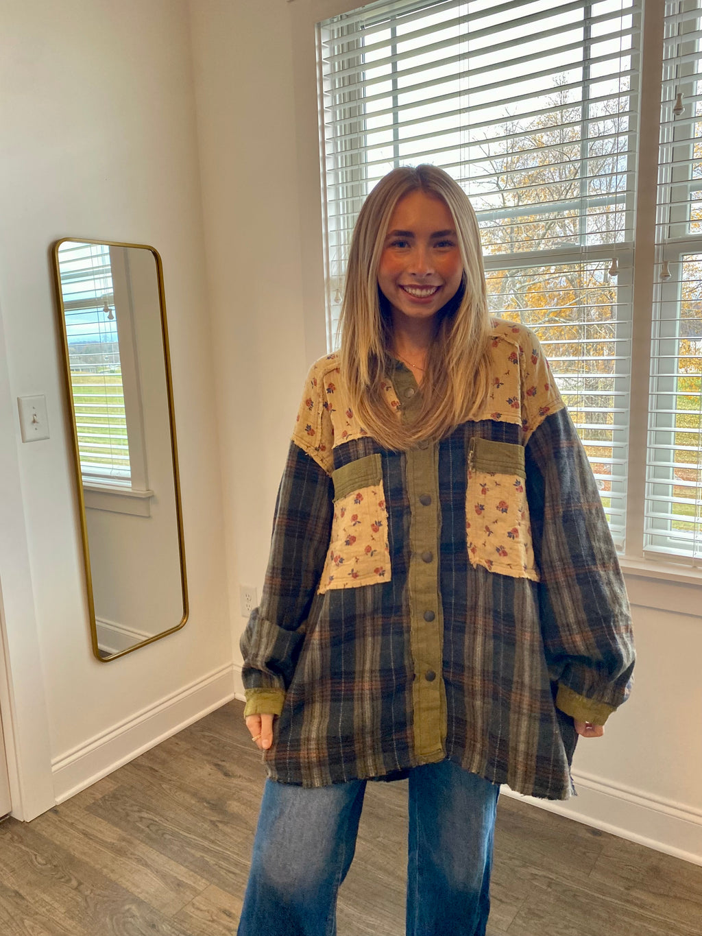 Woman wearing a plaid shirt with floral patches in a room with a window and mirror.