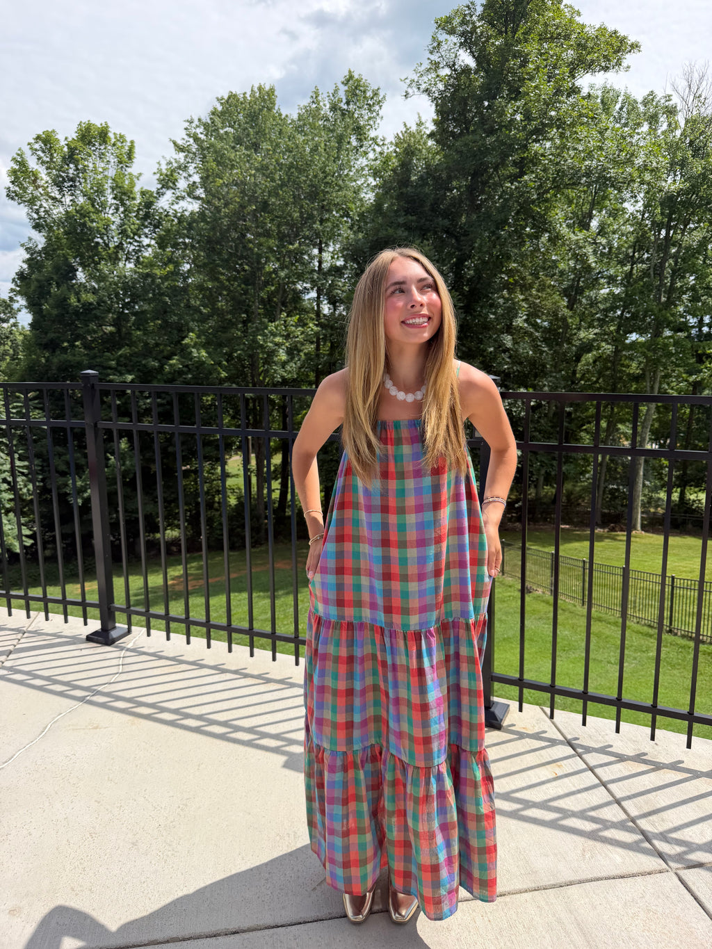 Woman in a plaid dress standing outdoors with trees in the background