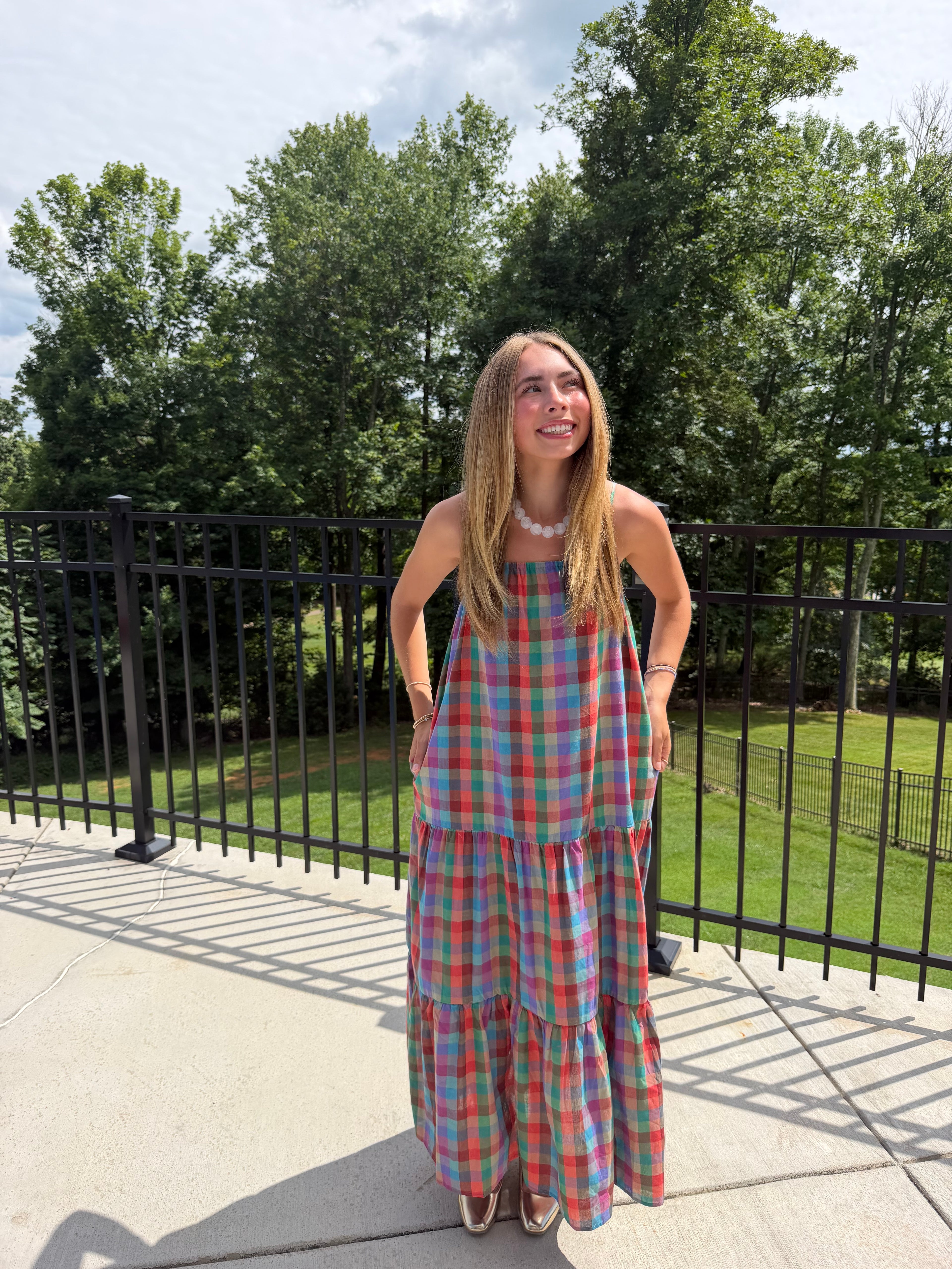 Woman in a plaid dress standing outdoors with trees in the background
