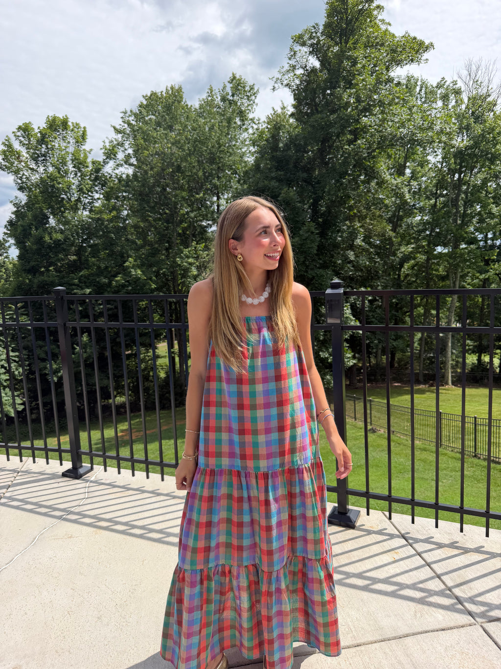 Woman in a colorful plaid dress standing outdoors with trees in the background