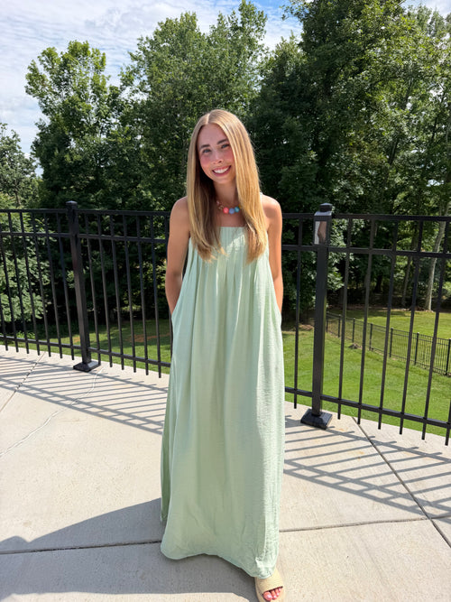 Woman in a light green dress standing outdoors with trees in the background