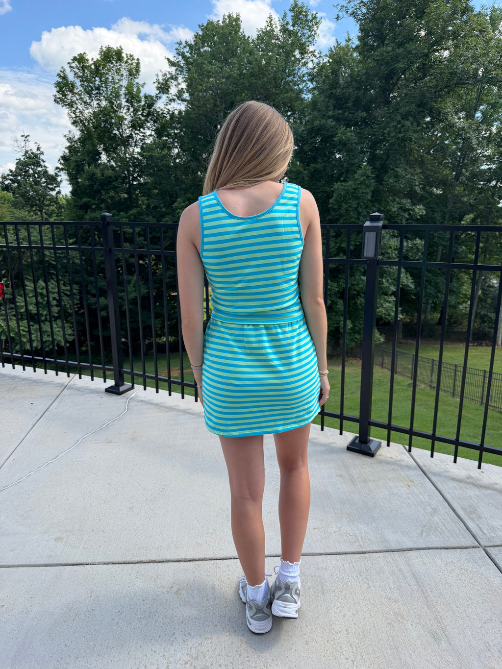 Person wearing a blue and green striped dress standing on a concrete surface with trees in the background.