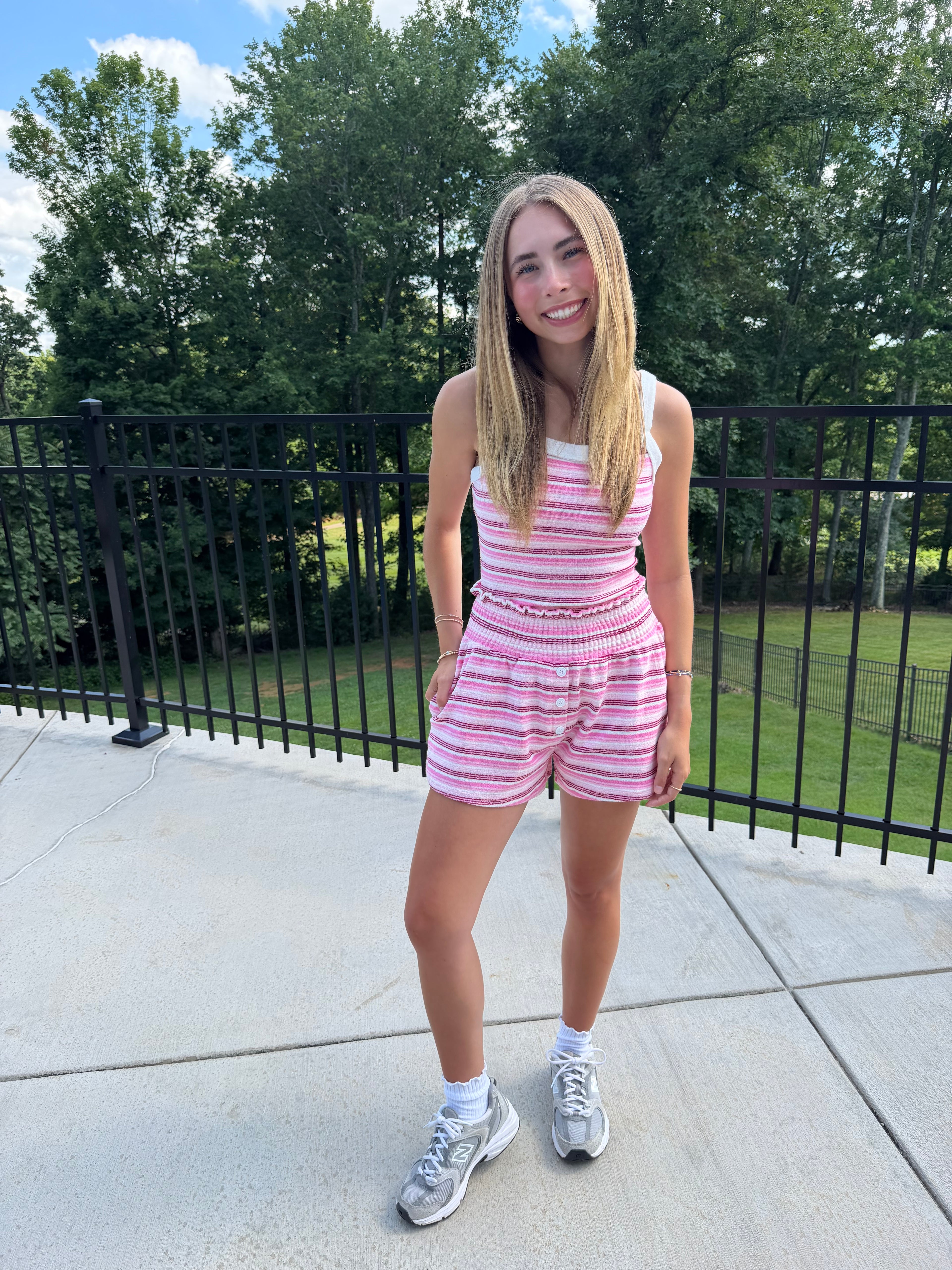 Young girl in a pink striped outfit standing outdoors with trees in the background