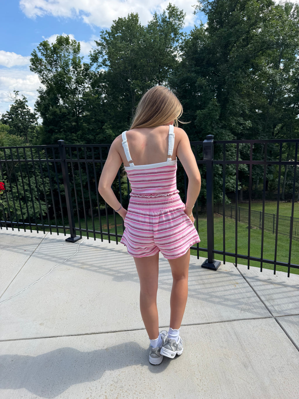 Person wearing a pink and white striped dress on a sidewalk with trees in the background