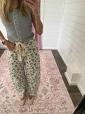 Person wearing floral pants and a gray top in a room with a pink rug and white walls.