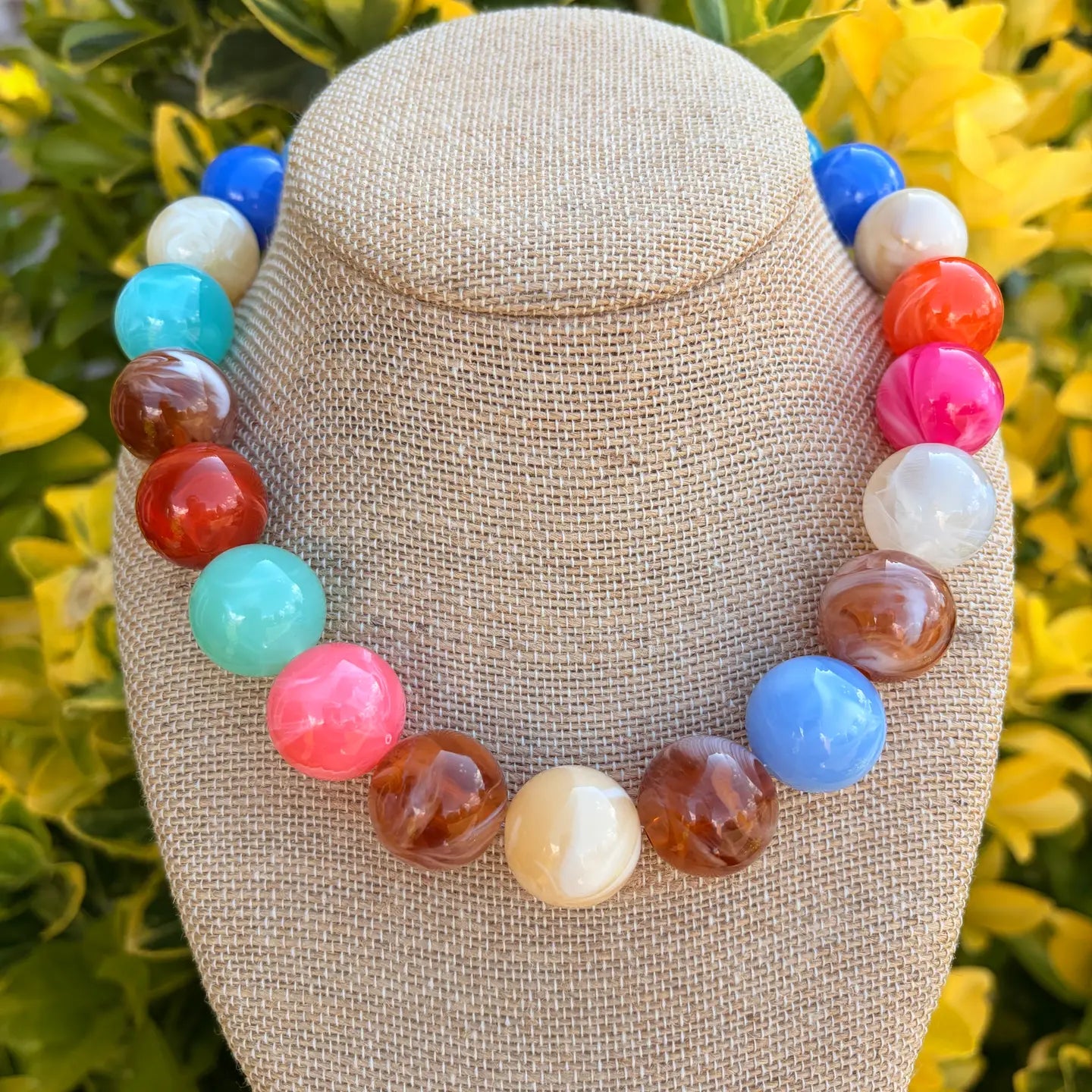 Colorful beaded necklace on a mannequin bust with a blurred floral background