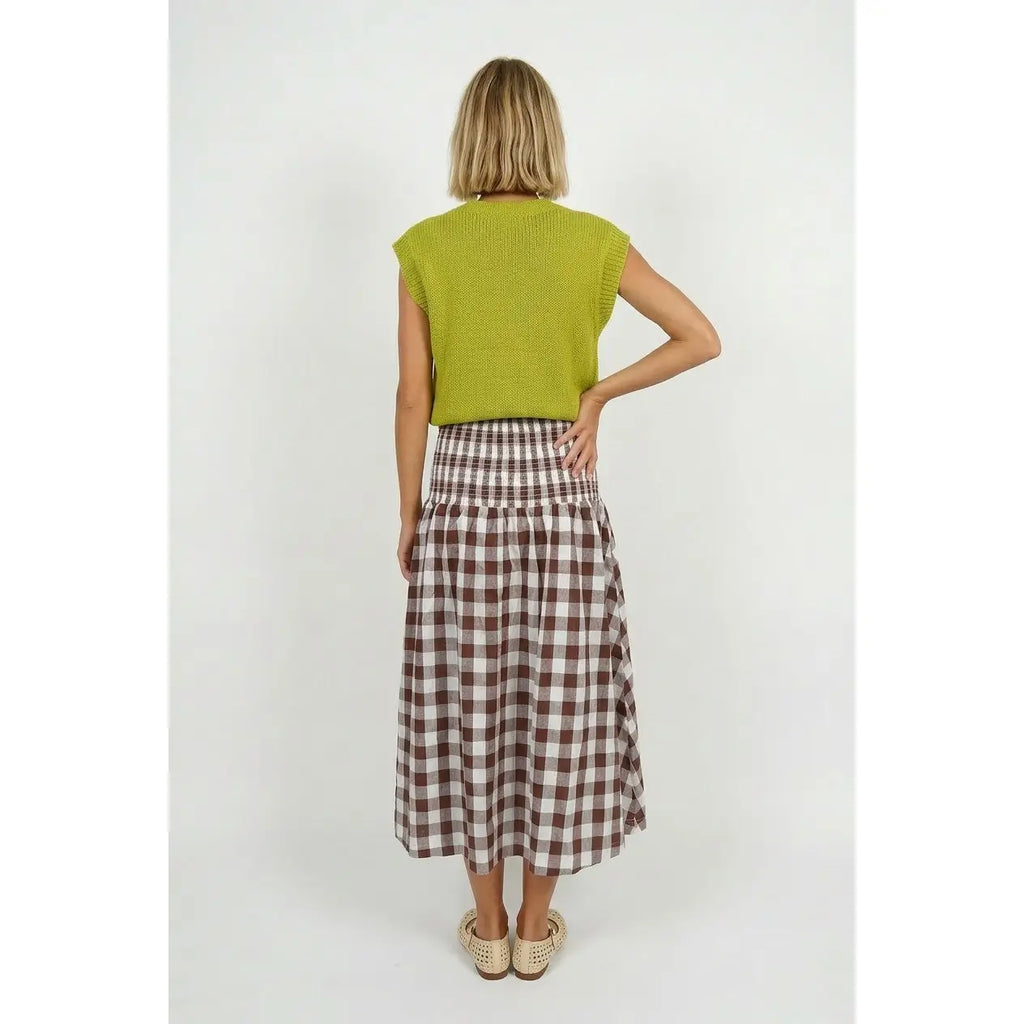 A woman viewed from the back wearing a bright yellow-green sleeveless knit top and a brown and white checkered midi skirt, paired with beige espadrille sandals, against a light gray studio background.