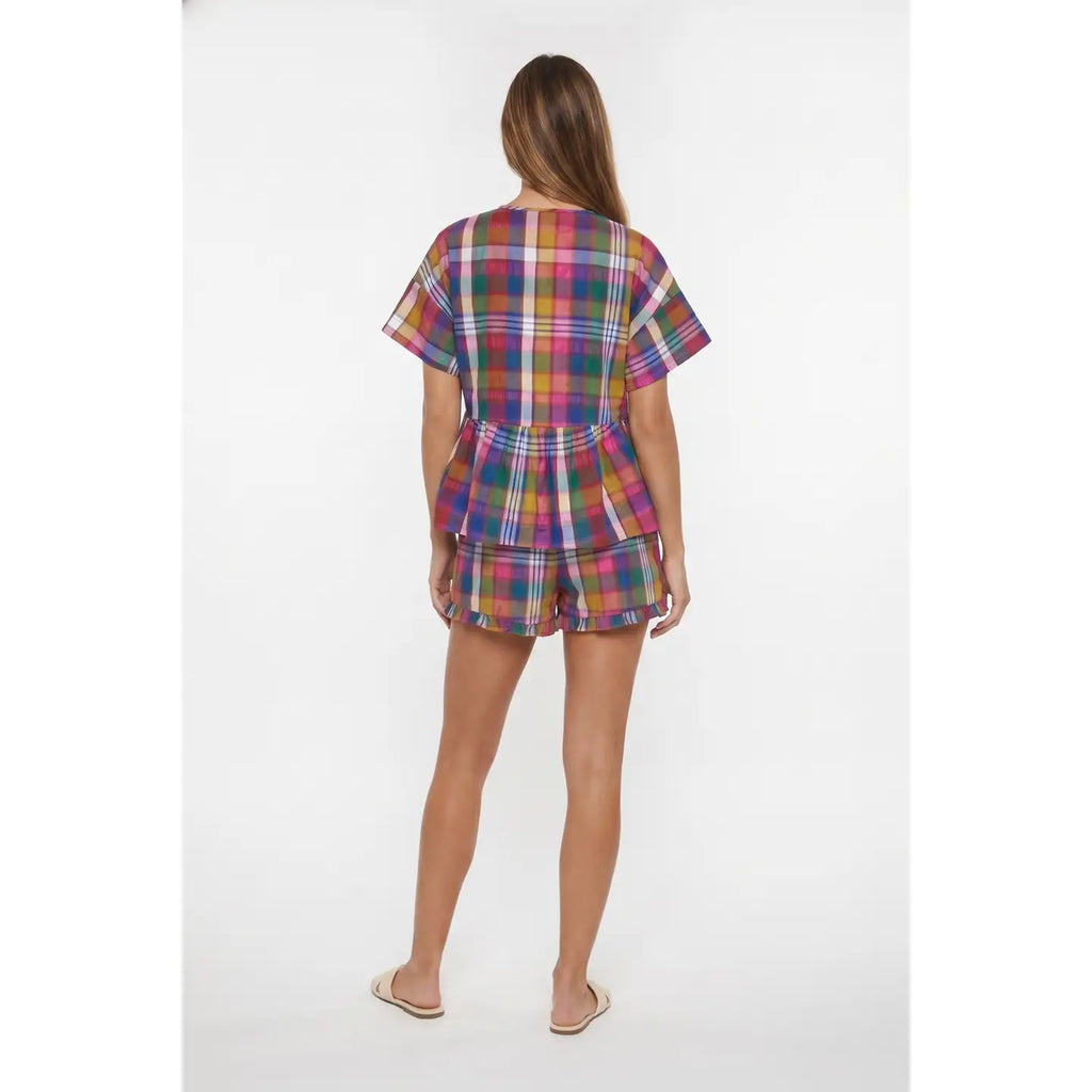 A woman viewed from behind wearing a short-sleeve plaid romper and matching shorts in a multicolor tartan pattern, standing against a plain white studio background.