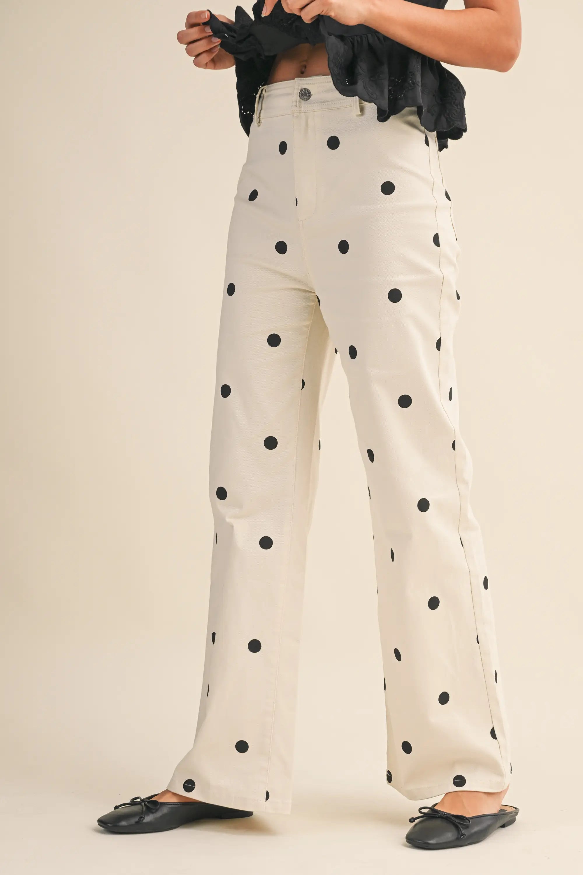 White pants with black polka dots worn by a person on a plain background