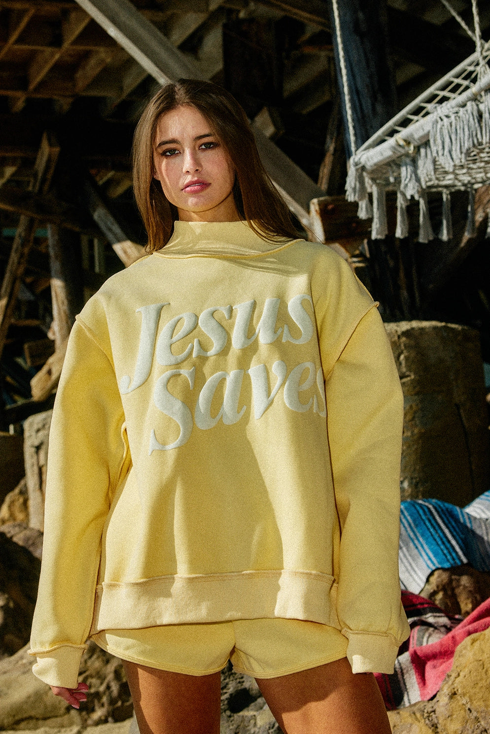 Person wearing a yellow 'Jesus Saves' sweatshirt in an indoor setting with wooden beams.