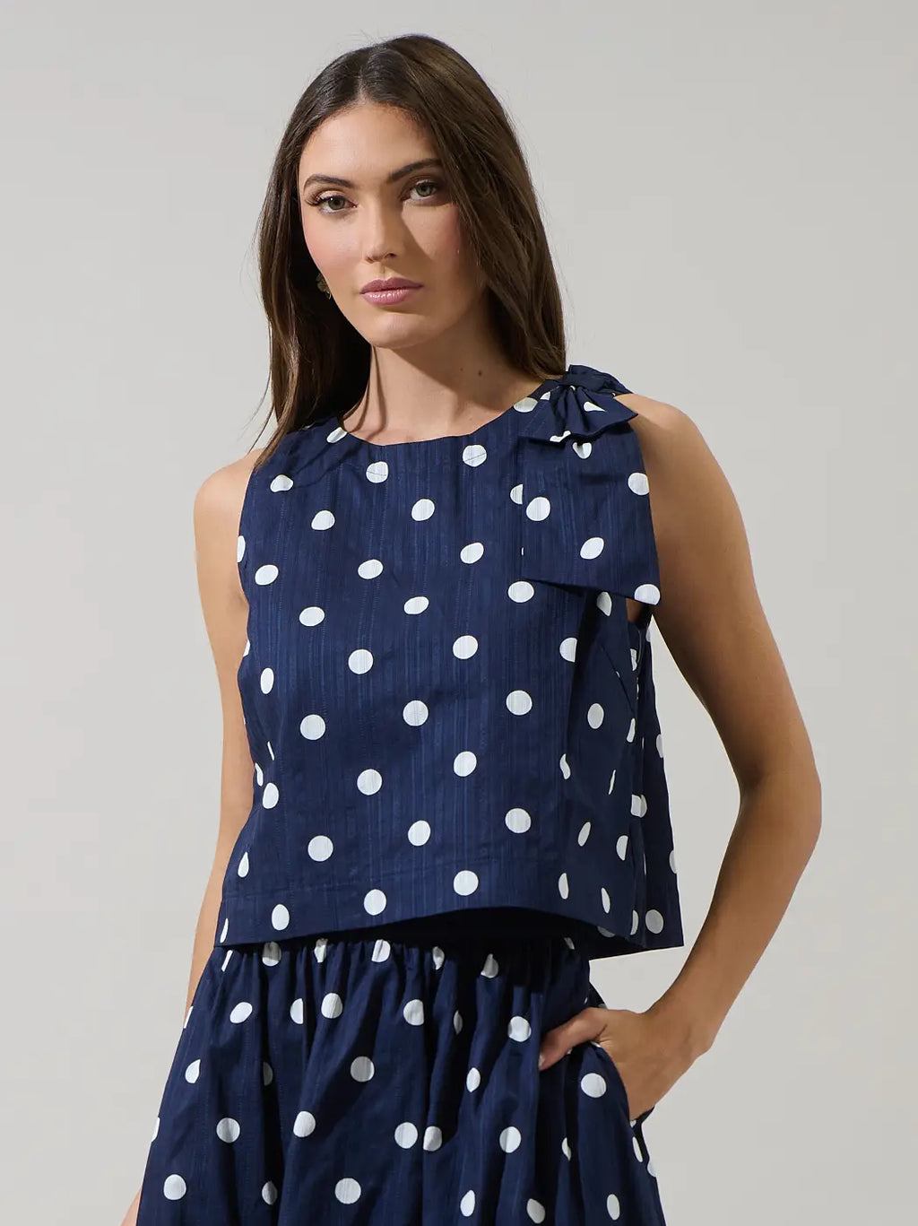 Woman wearing a navy blue top with white polka dots on a plain background
