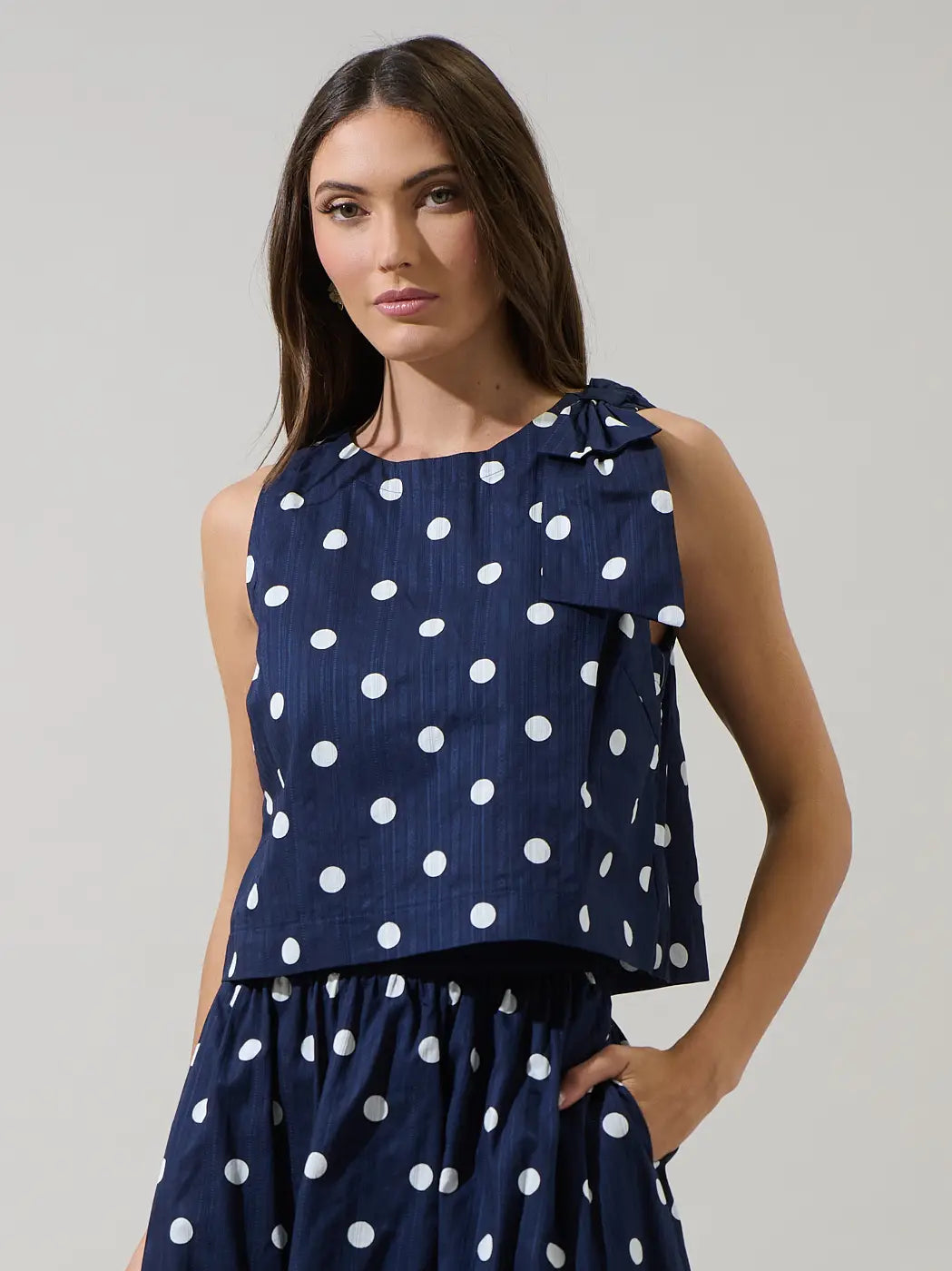 Woman wearing a navy blue top with white polka dots on a plain background