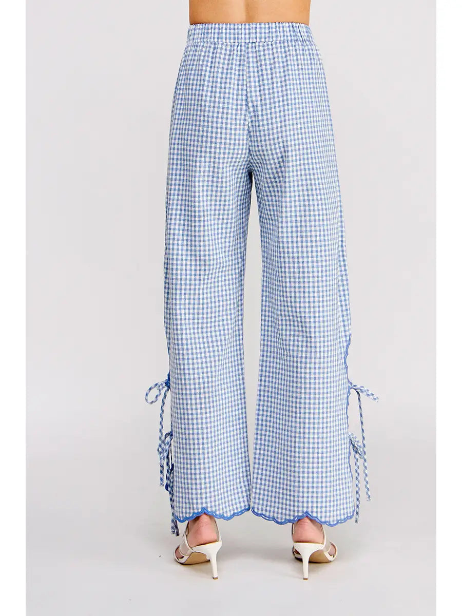 Blue and white gingham wide-leg pants with side tie details and scalloped hems, shown on a model from the back against a light gray background.