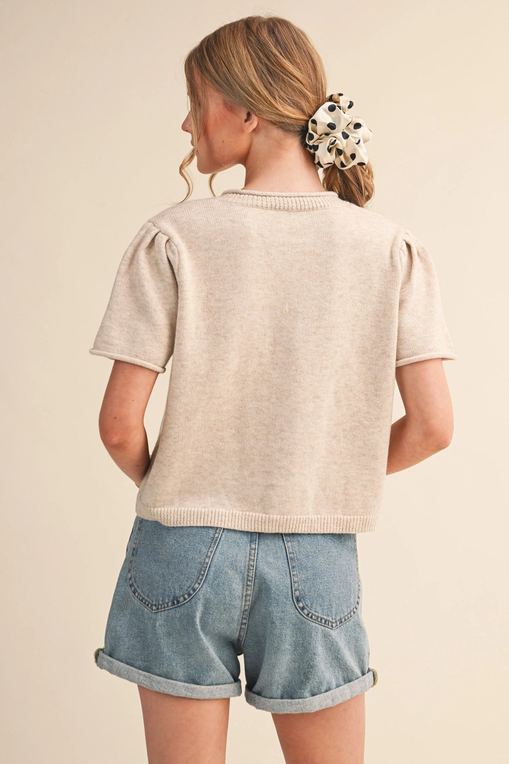 Person wearing a beige sweater and denim shorts on a beige background