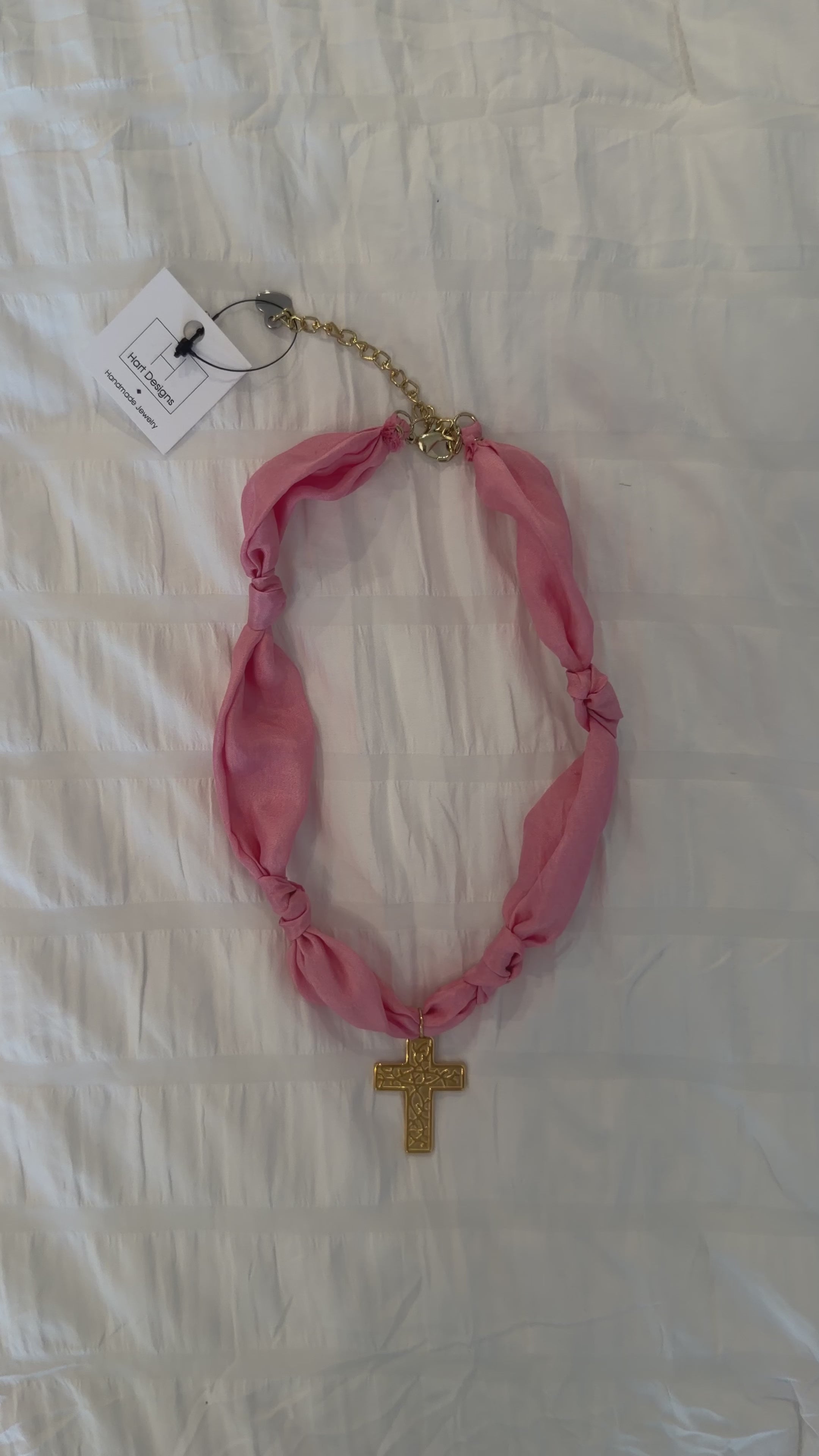 Pink scarf necklace with a gold cross on a white background