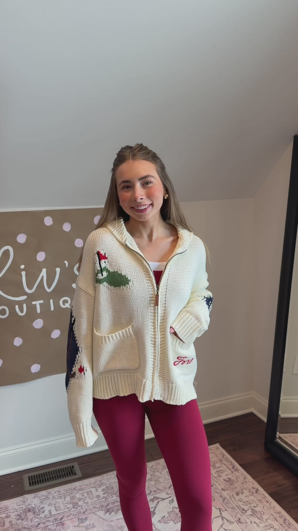 Person wearing a white sweater with green and red patterns, standing on a patterned rug.