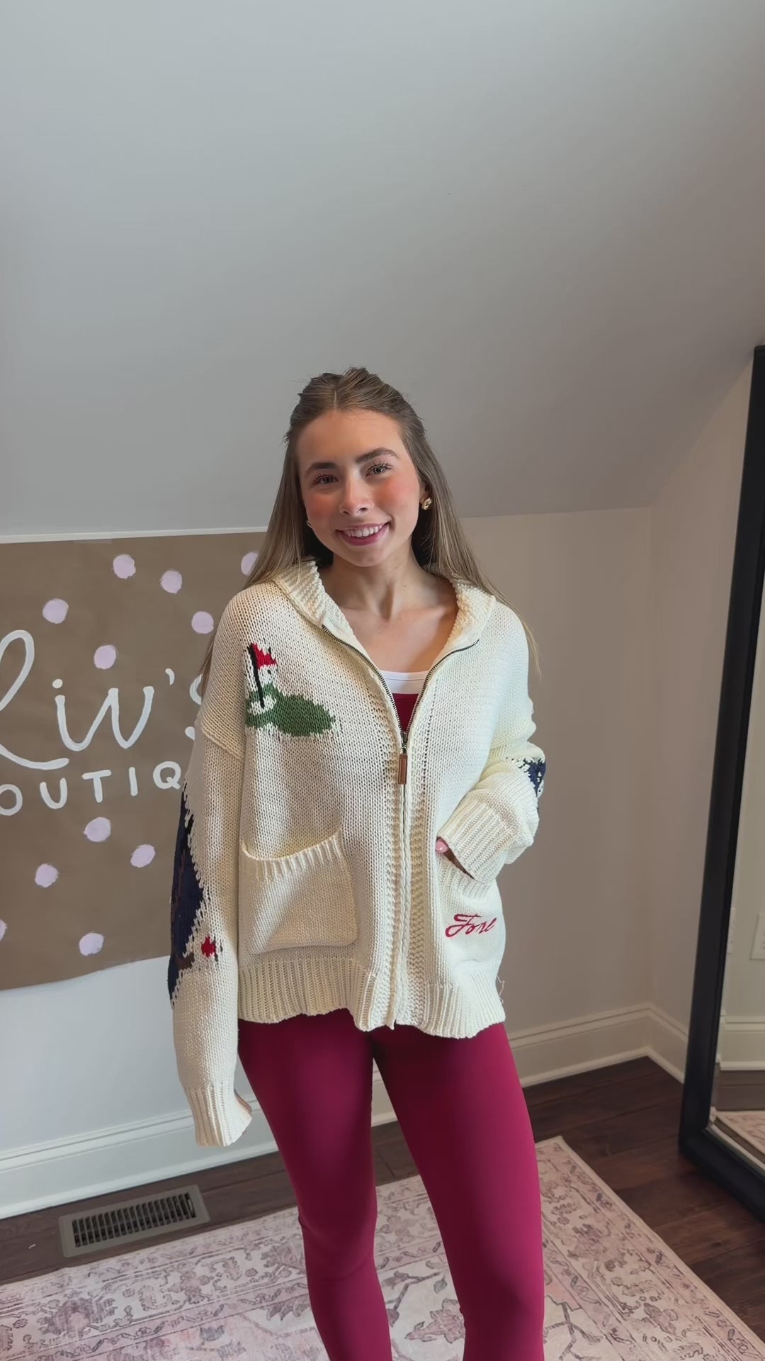 Person wearing a white sweater with green and red patterns, standing on a patterned rug.