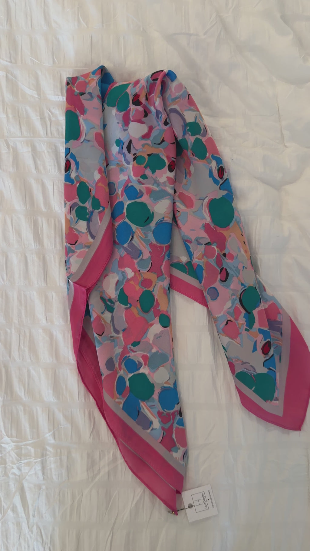 Colorful patterned scarf with pink accents on a white fabric background