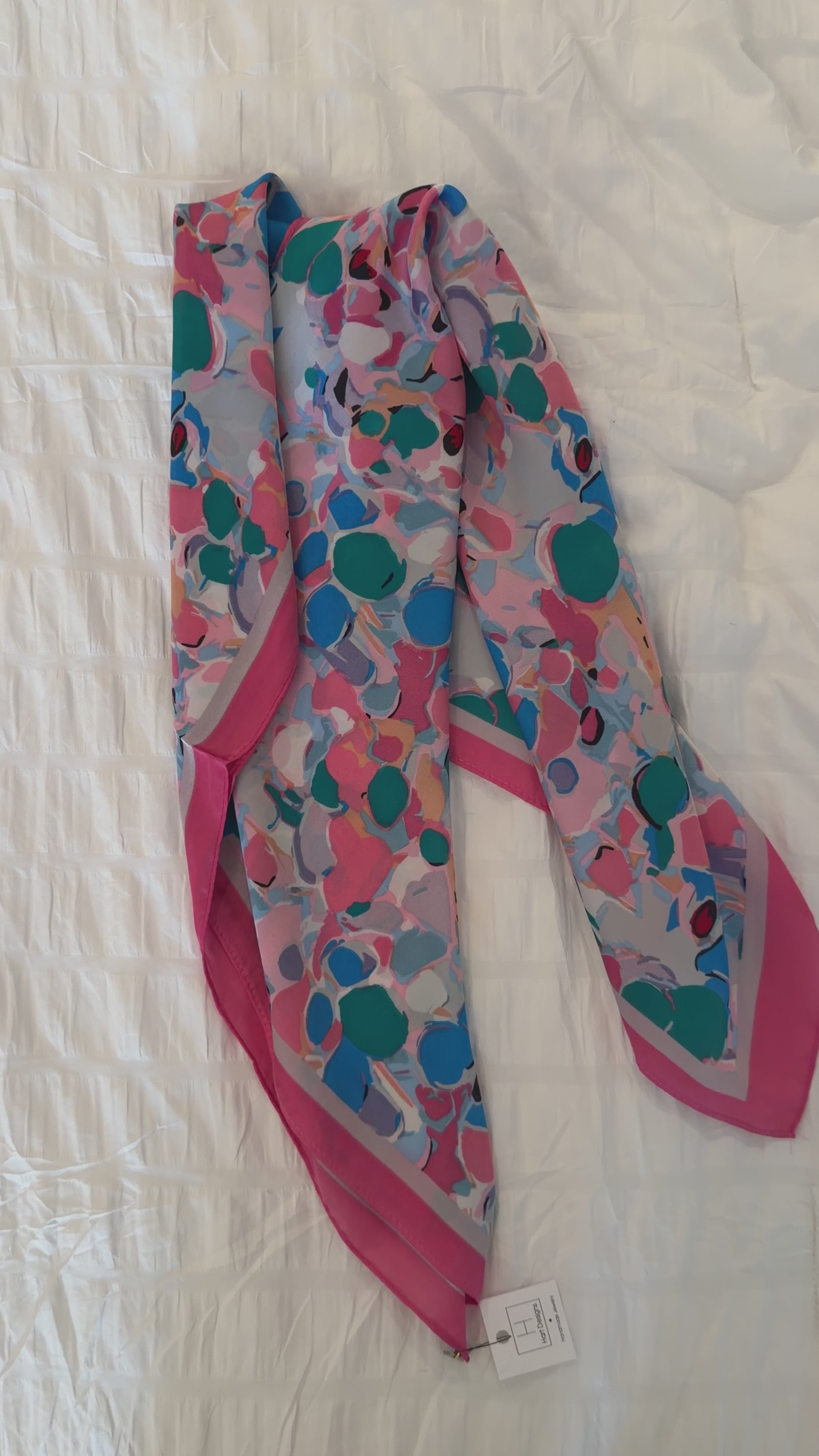 Colorful patterned scarf with pink accents on a white fabric background