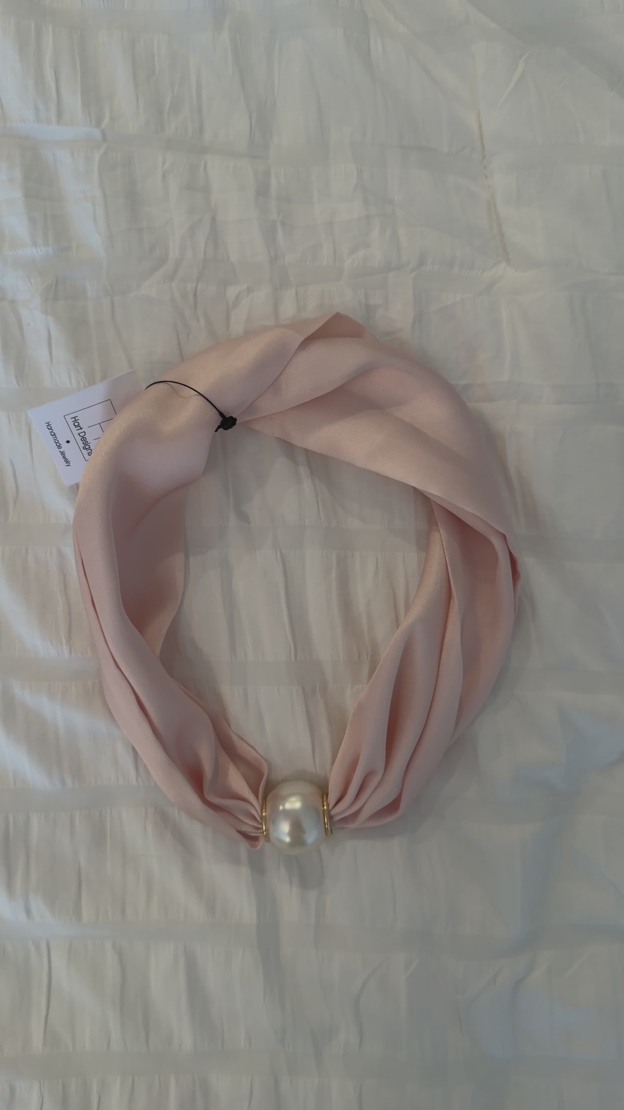 Pink scarf with a pearl-like bead on a white textured background