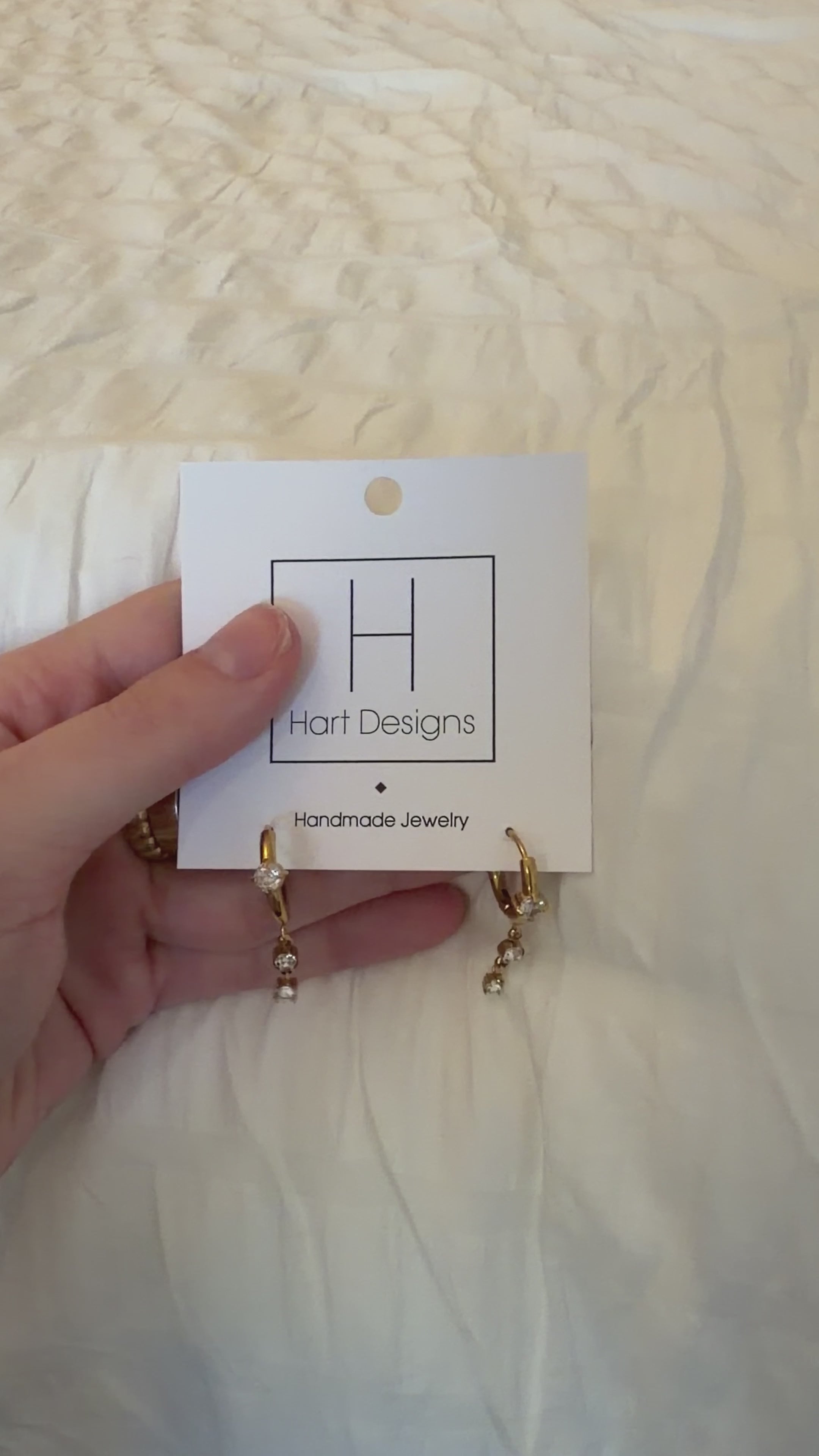 Hand holding a pair of gold earrings with a white card on a textured white background